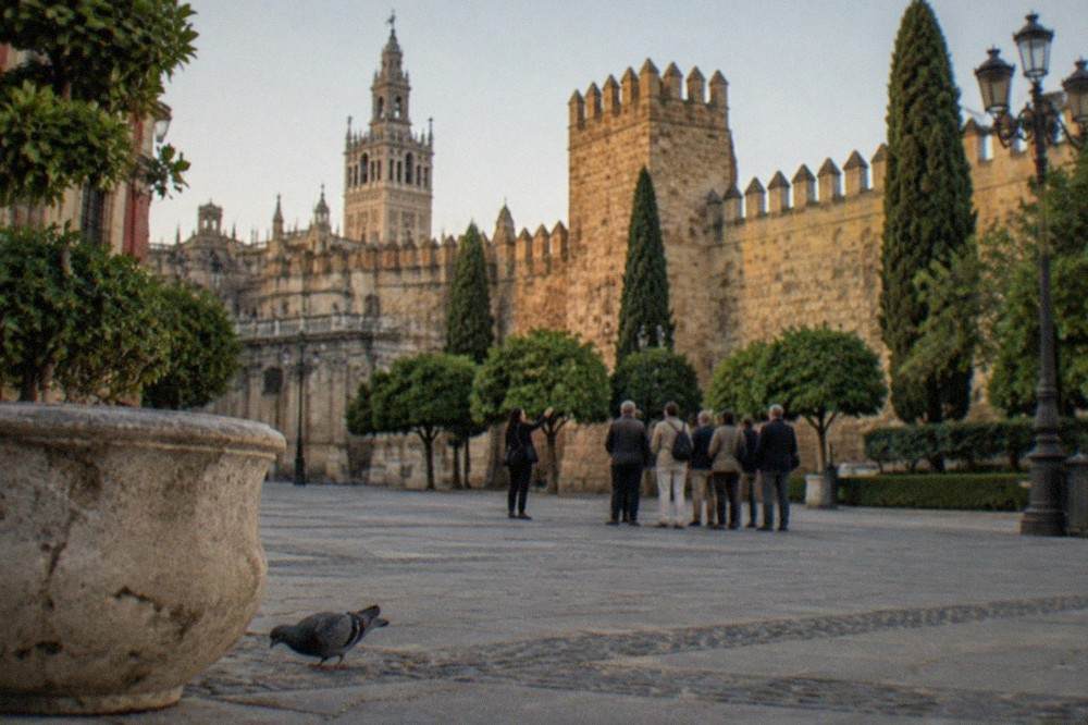 A guide speaking to a gathering of visitors beside a historic Seville building