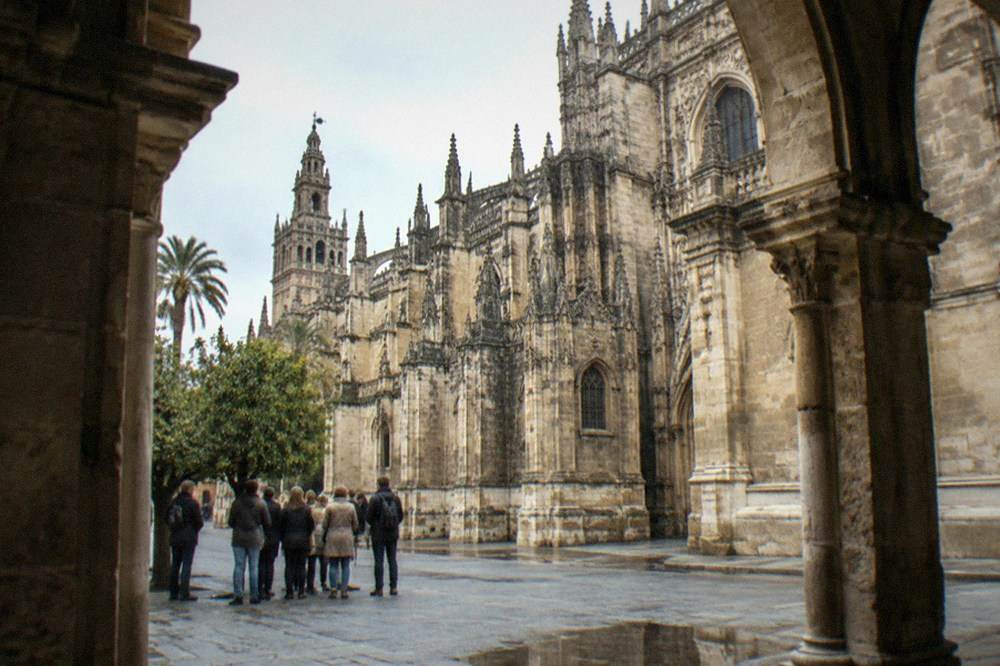 Visitors gathered in a Seville square while a guide gestures toward a historic facade