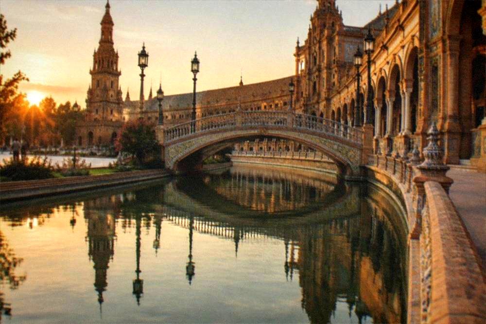 The tiled bridge and colonnade of Plaza de España reflected in its canal at golden hour