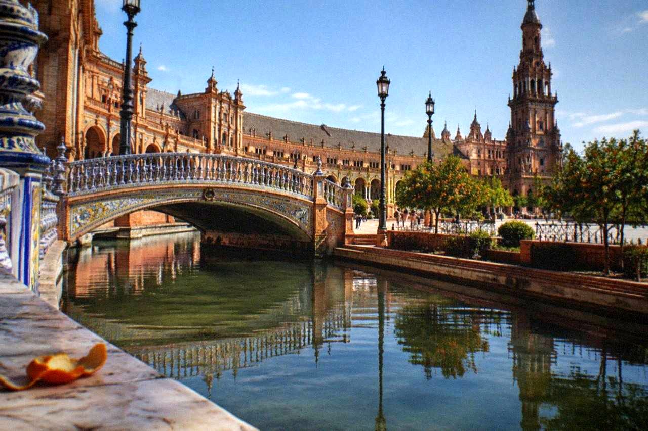 A sunlit Seville plaza with orange trees, tiled benches and historic facades