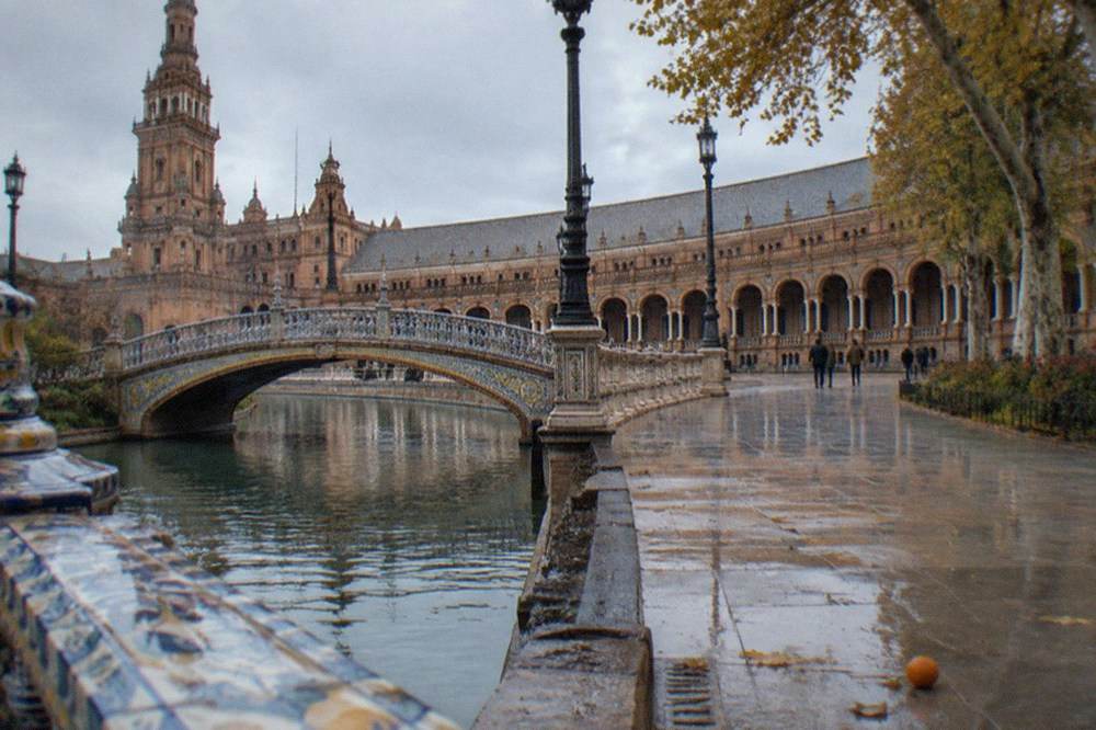 Open plaza with tiled benches and a bridge arching over a canal in Seville