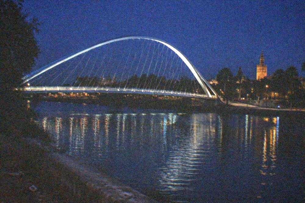 Illuminated bridge and riverside walkway reflected in the Guadalquivir at dusk in Seville