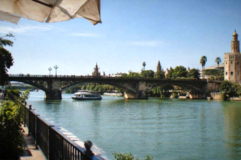 The Guadalquivir riverfront in Seville with a stone bridge and a riverside walkway