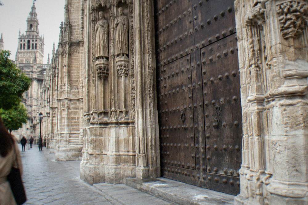 Stone doorway of Seville Cathedral with carved arches and a set of wooden doors