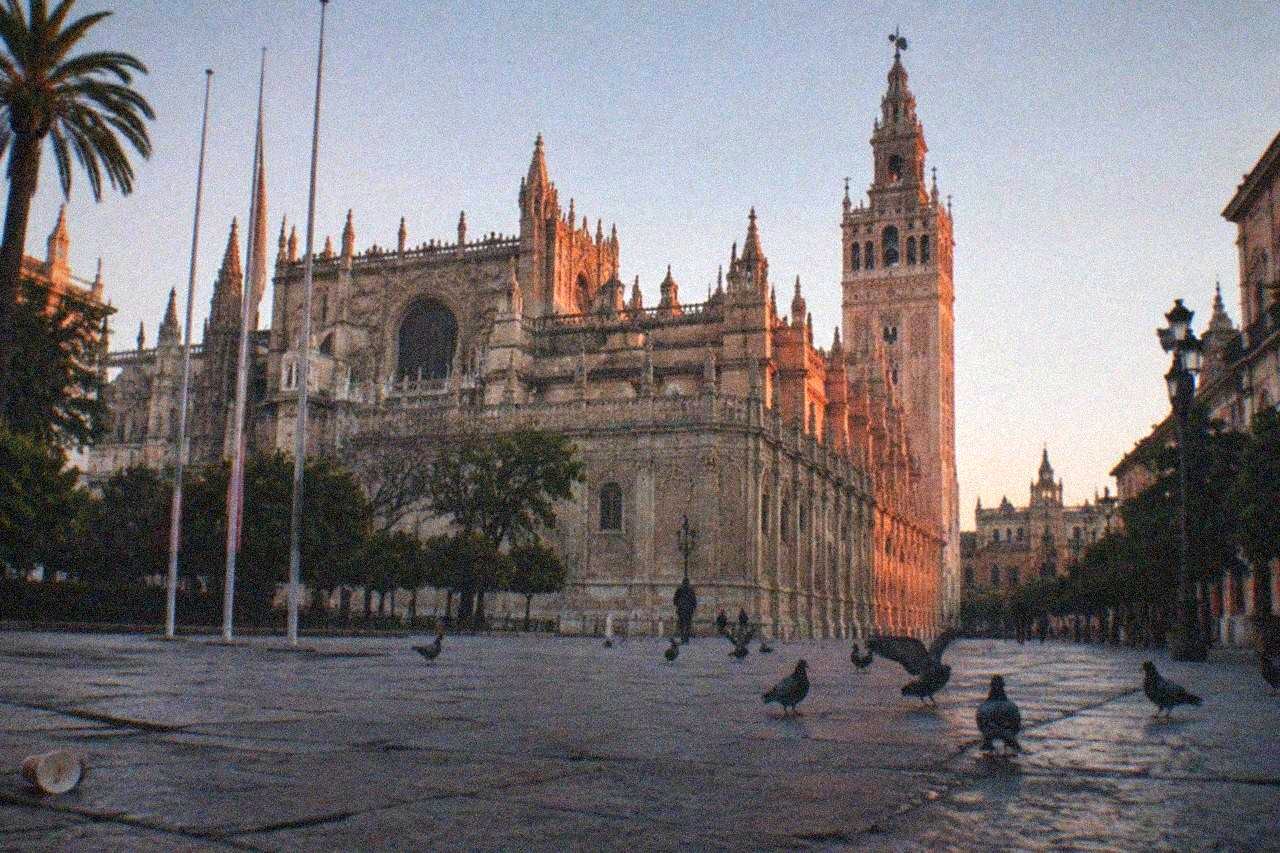 Gothic cathedral facade rising above a wide stone plaza in Seville under a clear sky