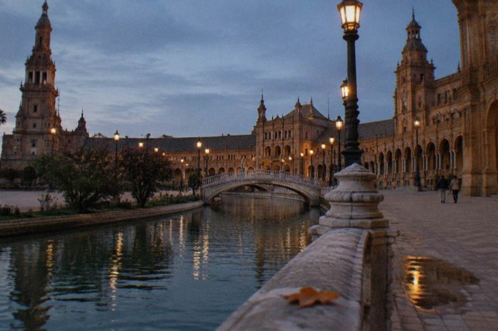 Lampposts and stone arcades along an empty plaza in Seville after sunset