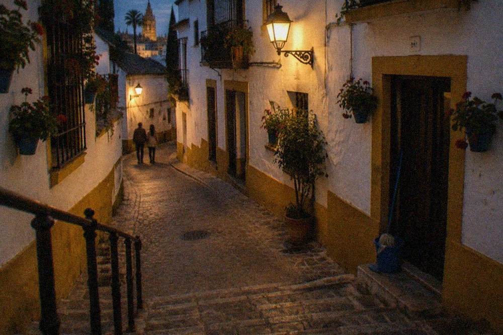 Narrow lamp-lit lane with white walls in the Santa Cruz quarter at dusk
