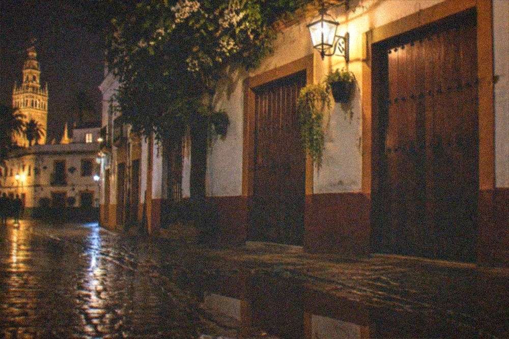 Empty street corner with shuttered doors and a lit sign in Seville at night