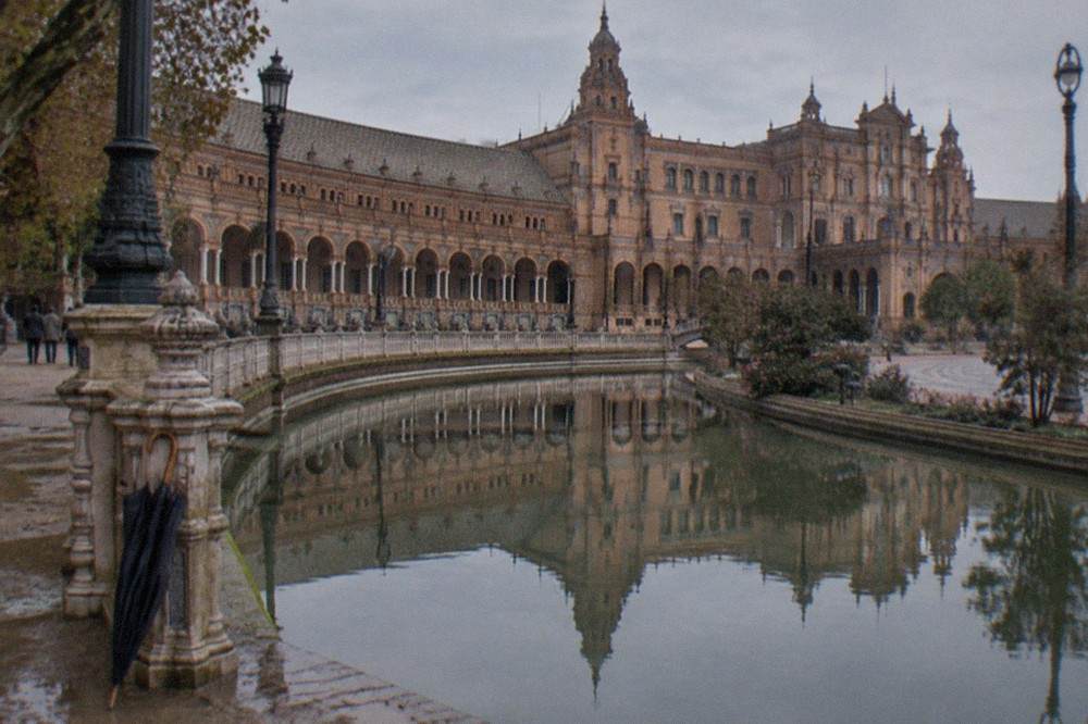 The semicircular brick facades of Plaza de España reflected in the still water of its canal