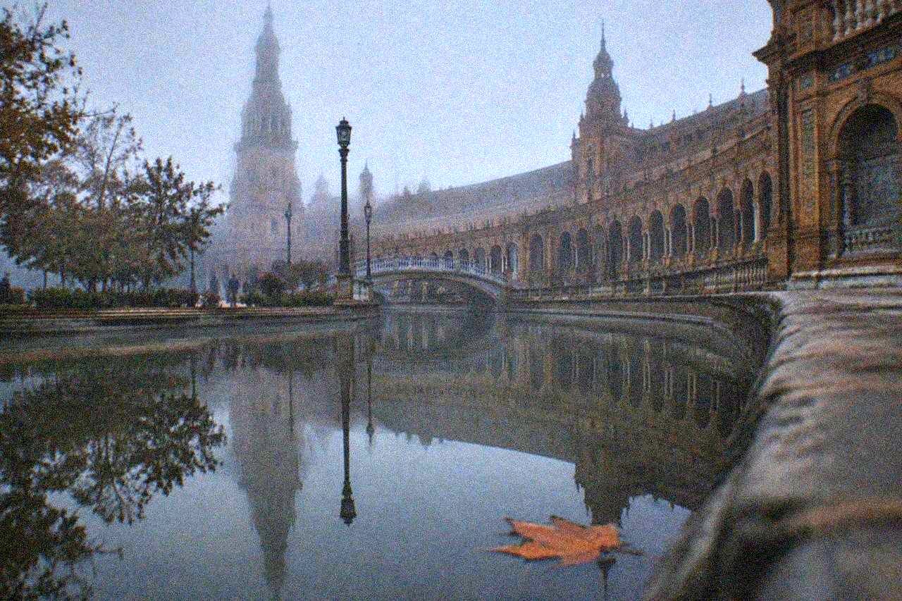 The semicircular brick buildings of Plaza de España reflected in the still water of its canal