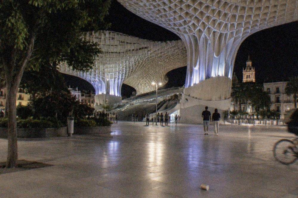 A lit public square in Seville at night with lamps reflecting on stone paving
