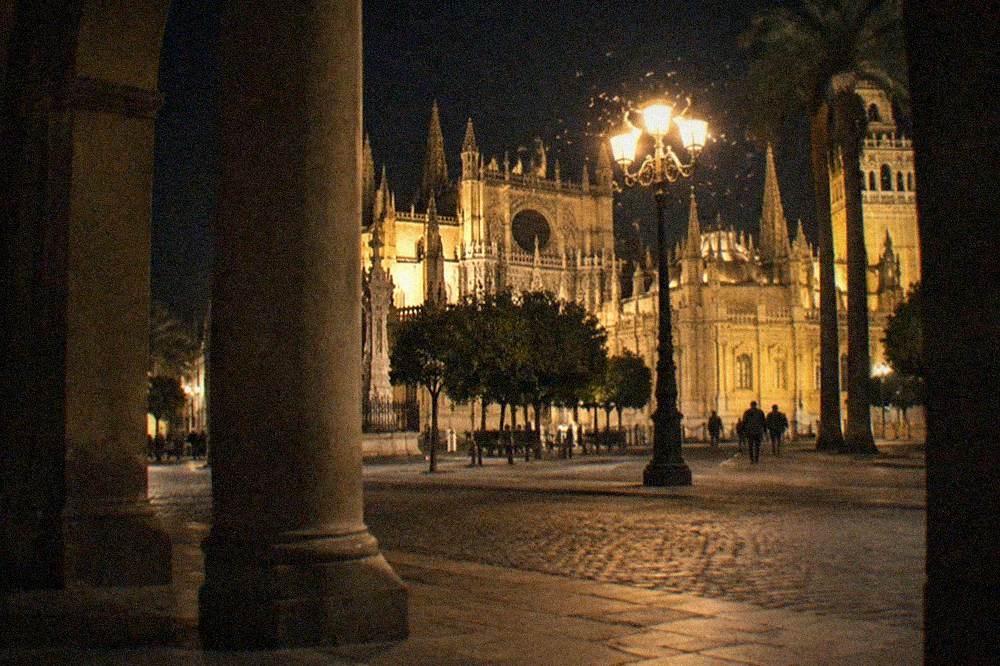 The illuminated facade of Seville Cathedral seen from a dark plaza at night