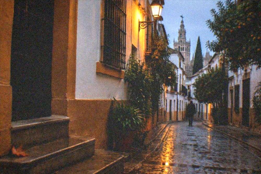 Warm street lamps glowing over an empty Seville street in the evening