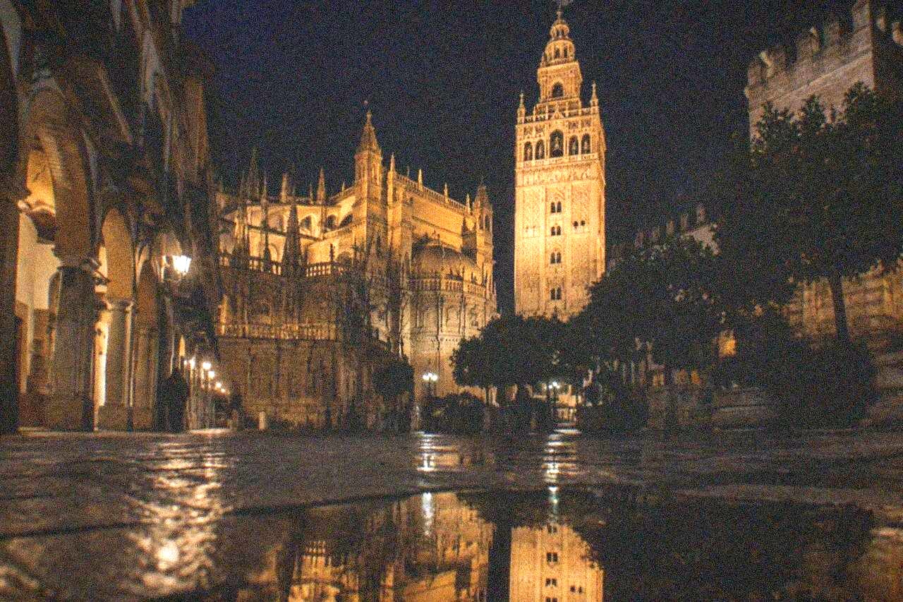Seville Cathedral and the Giralda tower illuminated against a dark evening sky