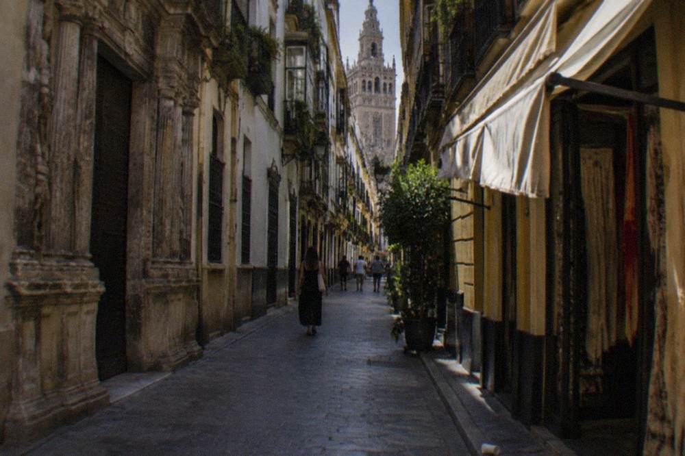 A historic Seville street with tall shaded buildings and a stone facade
