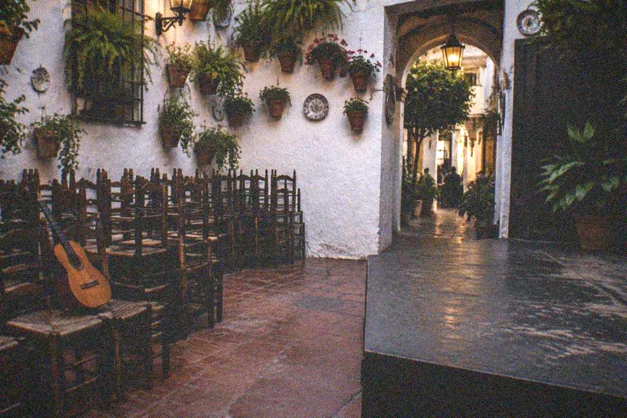 Empty flamenco stage with wooden chairs and a guitar resting against a wall