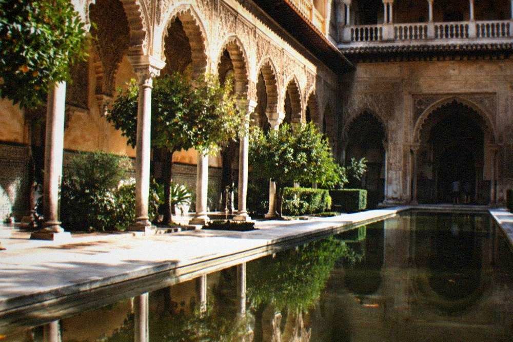 Sunlit arcade of arched doorways facing a long reflecting pool