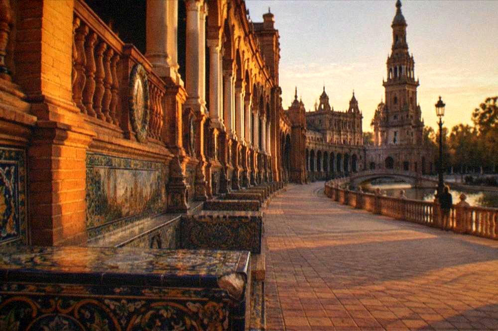 Crowd-free colonnade with tiled benches curving along a Seville square at golden hour