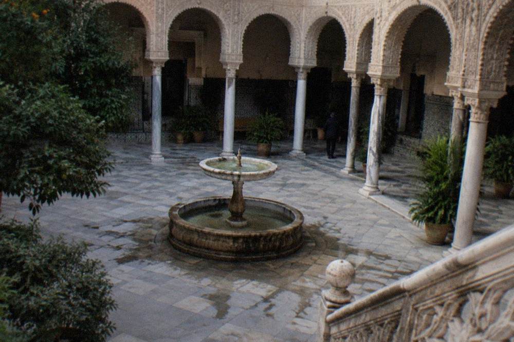 A tiled palace courtyard with arches and a stone fountain