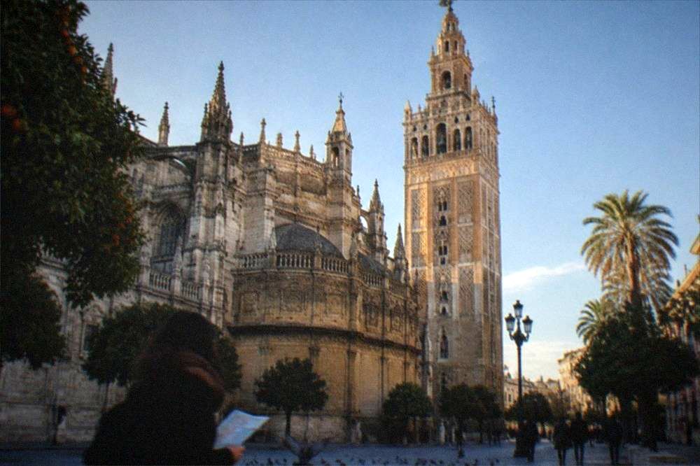 A city square with a cathedral facade and a tall bell tower
