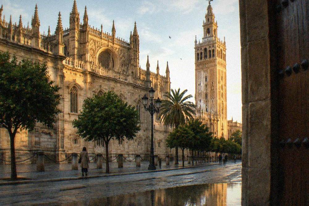 Ornate gothic cathedral facade with a weathered stone bell tower above Seville rooftops