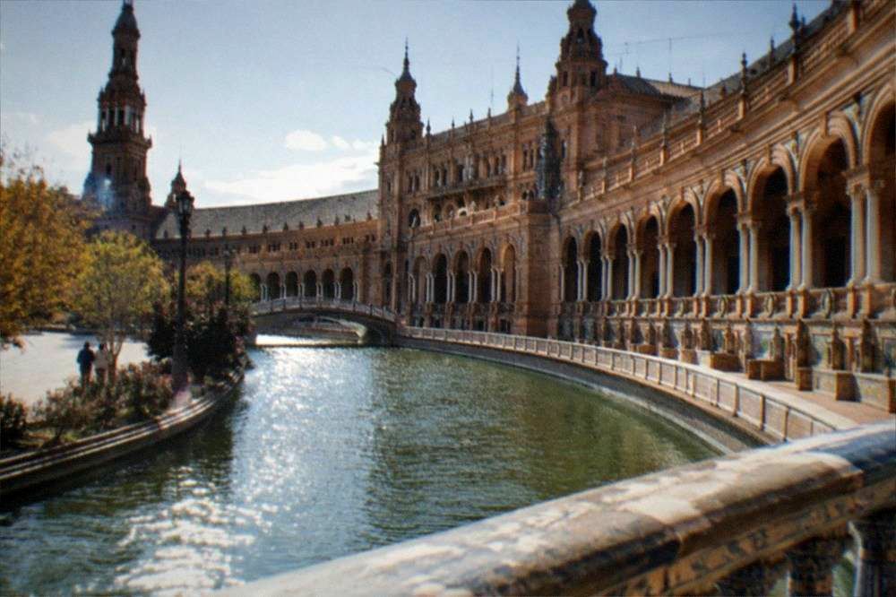 Semicircular plaza with coloured tiled alcoves and a bridge over a canal