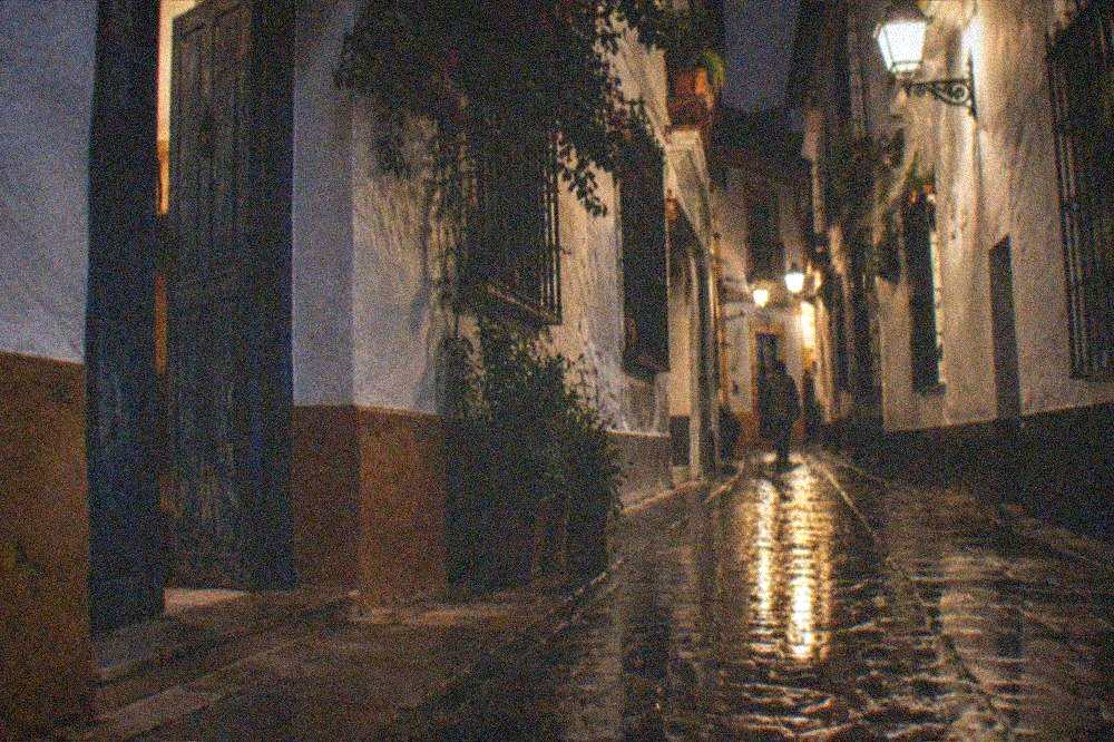 Evening lit narrow street with old wall lamps in Seville