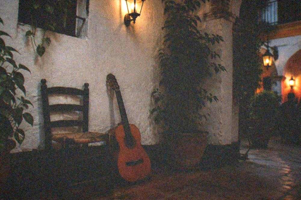 A dim flamenco stage with a wooden chair and a guitar resting against the wall