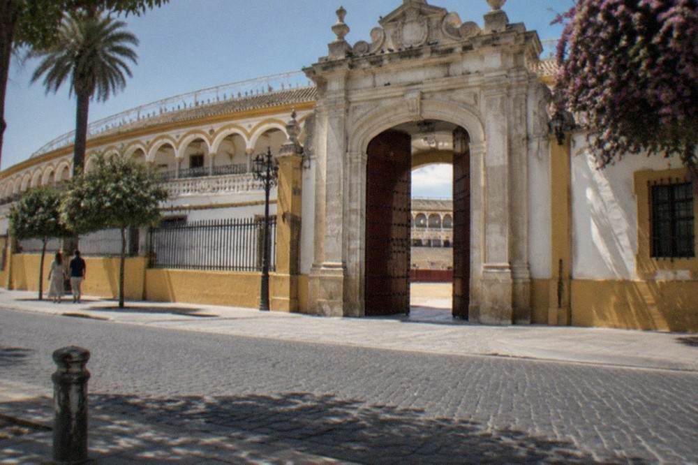 The arched stone facade and entrance gates of the Seville bullring under a clear sky