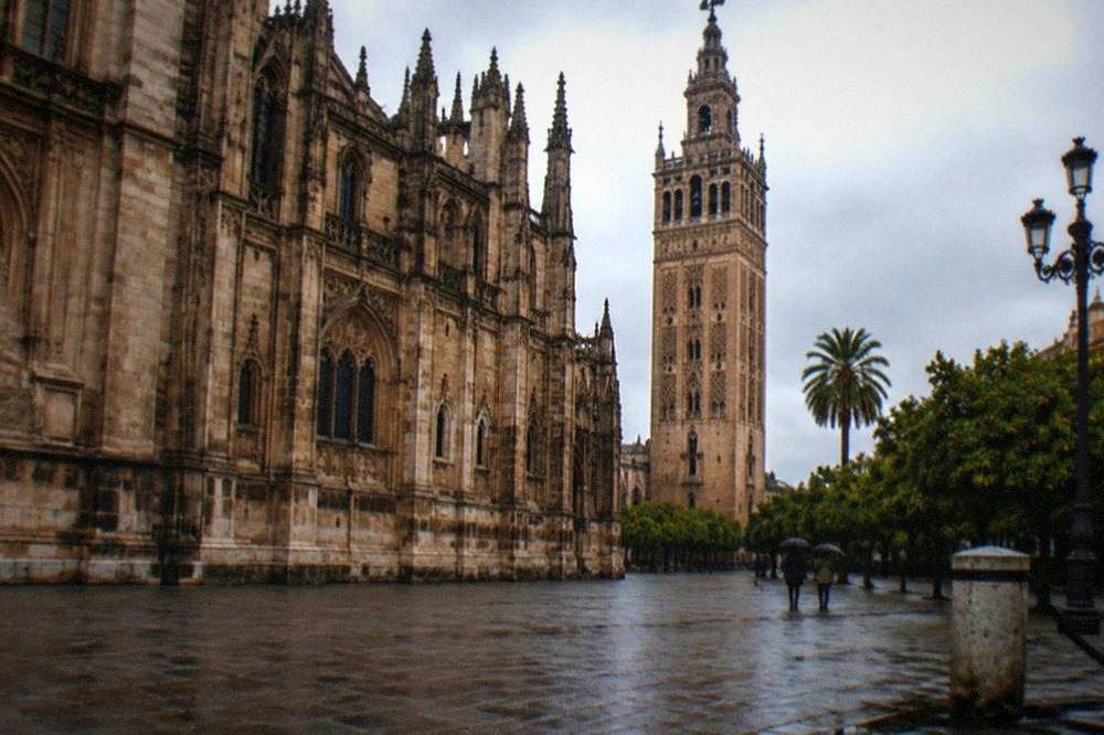 An open square beside Seville Cathedral with the Giralda rising behind, empty in the late afternoon