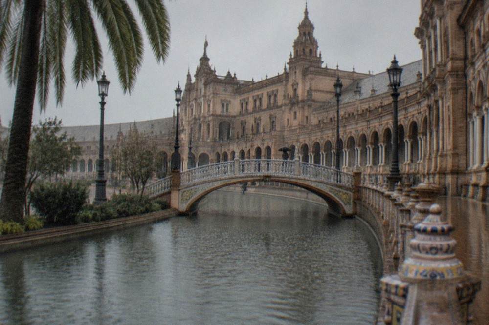 A wide Seville plaza with arcades and a canal in winter light