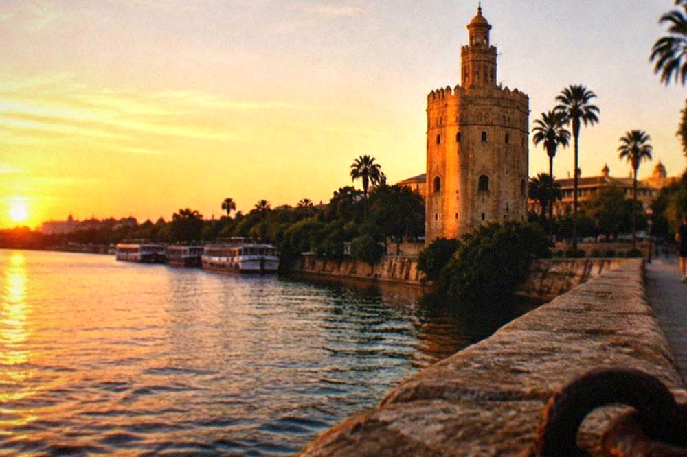 Torre del Oro de piedra dorada junto al río Guadalquivir al anochecer
