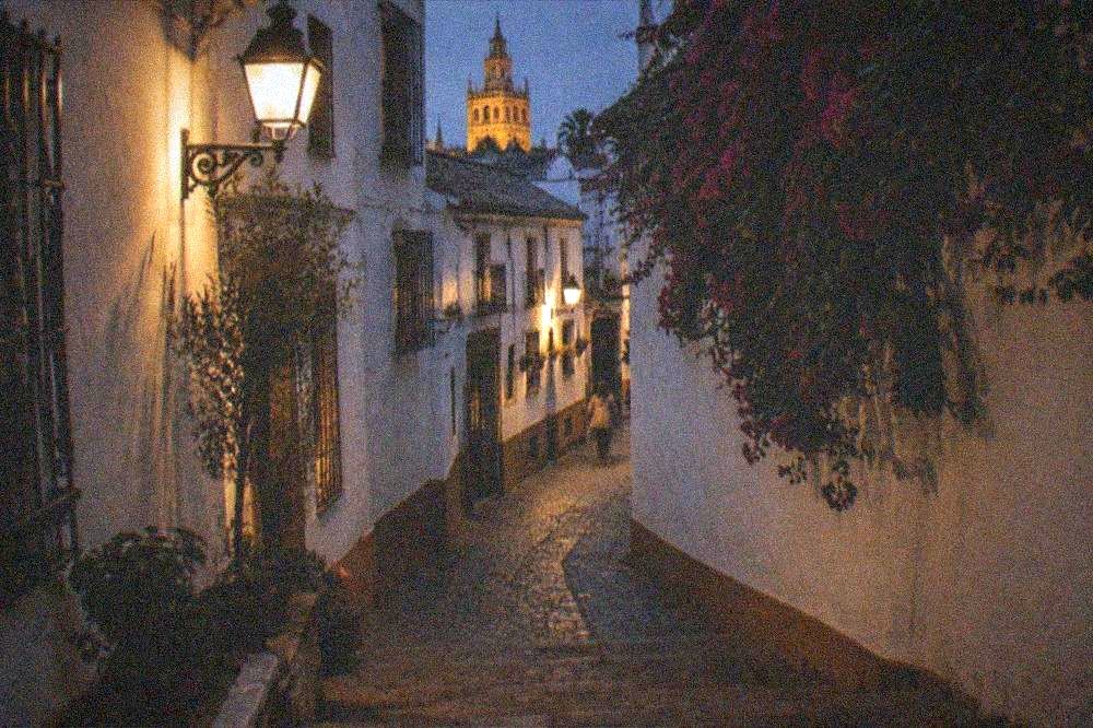 Callejuela iluminada por faroles y paredes encaladas en el barrio de Santa Cruz de noche